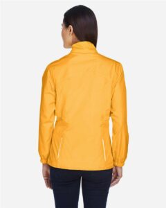 CORE365 78183 Women’s Techno Lite Motivate Unlined Lightweight Jacket – Campus Gold (on model back)